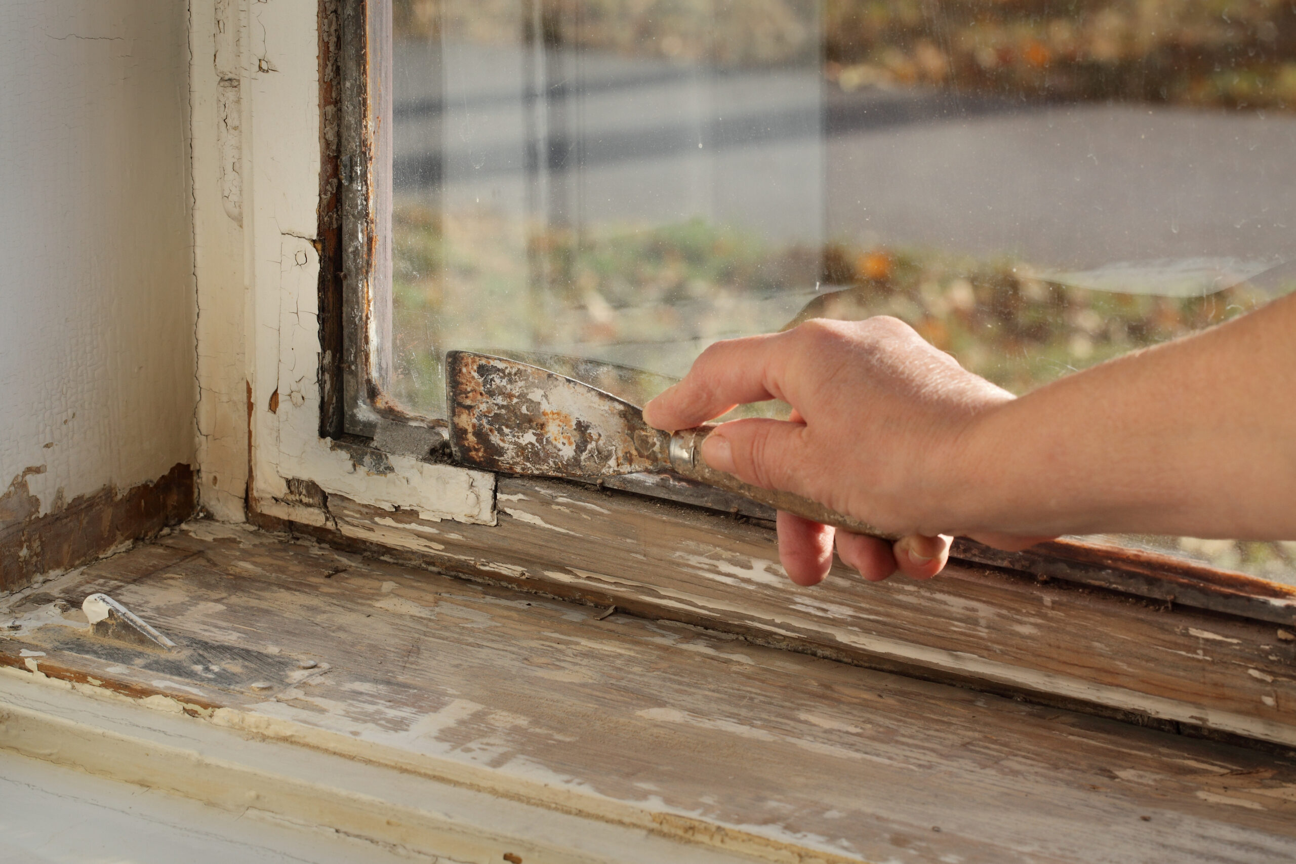 Worker removing oil window glazing putty using putty knife tool, old window restoration.