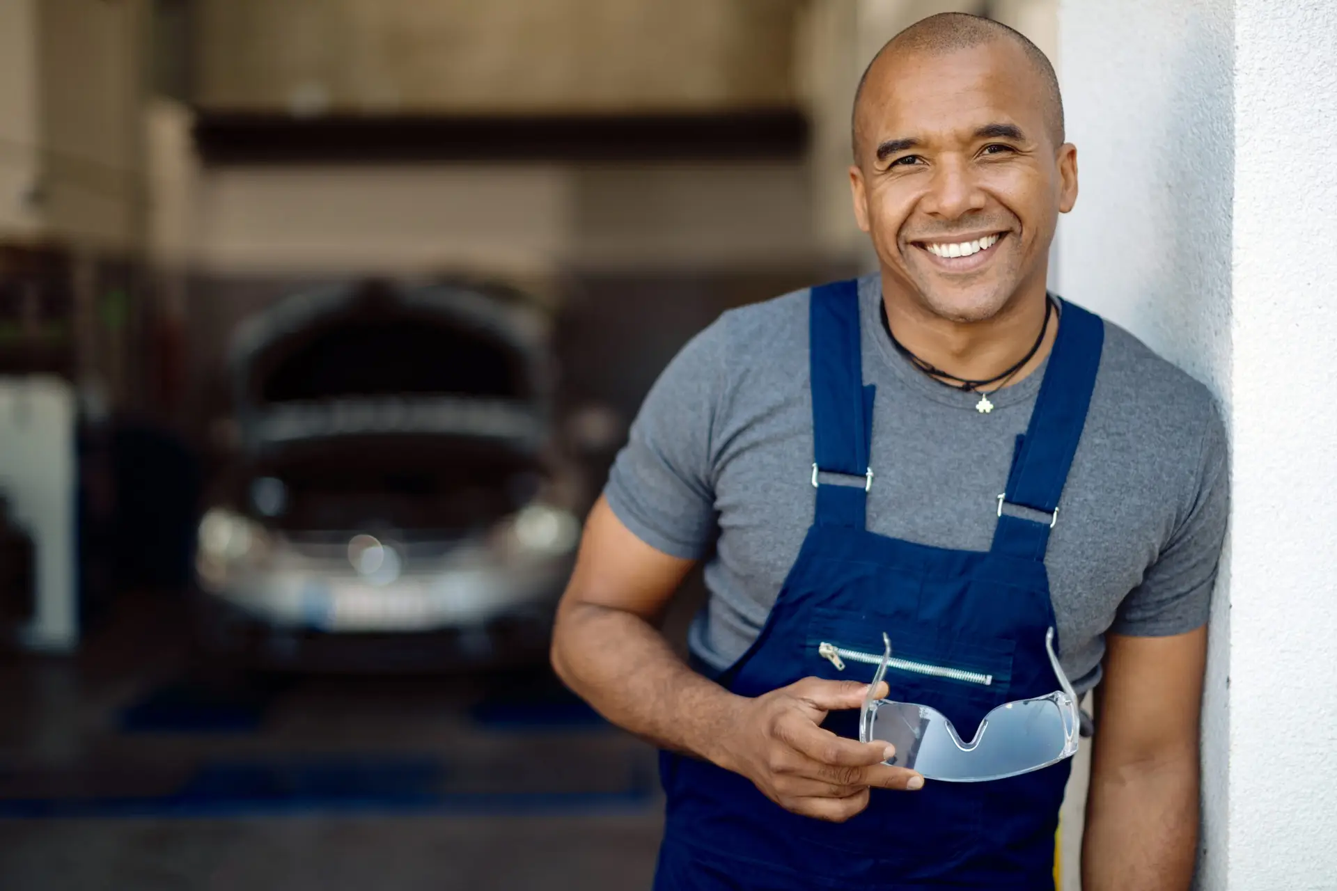 Portrait of happy black auto repairman standing in a workshop and looking at camera.