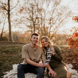 Young couple pose in a field with a bright golden hour behind them.